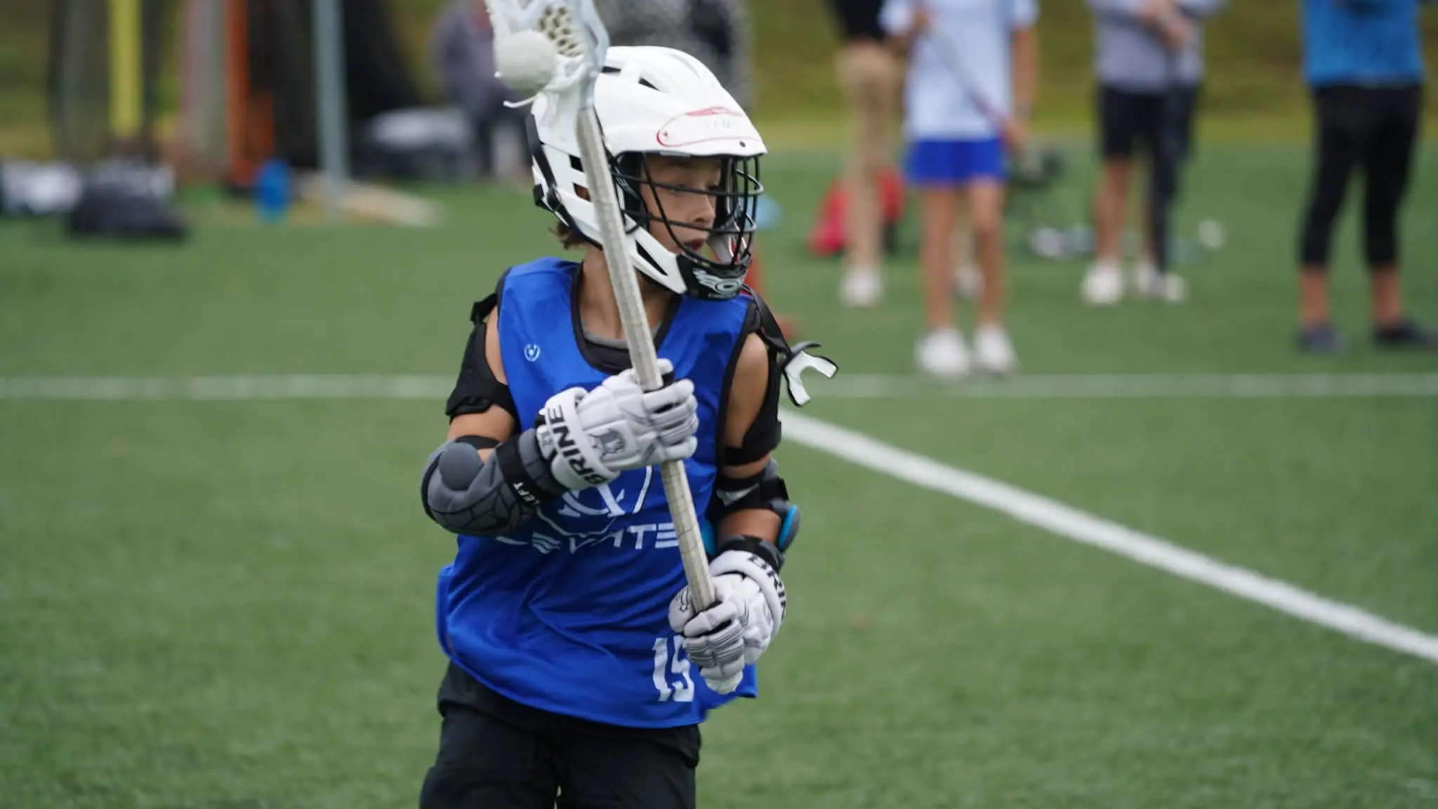 A KC Elevate youth player in the blue Elevate jersey, stick up, ready to catch