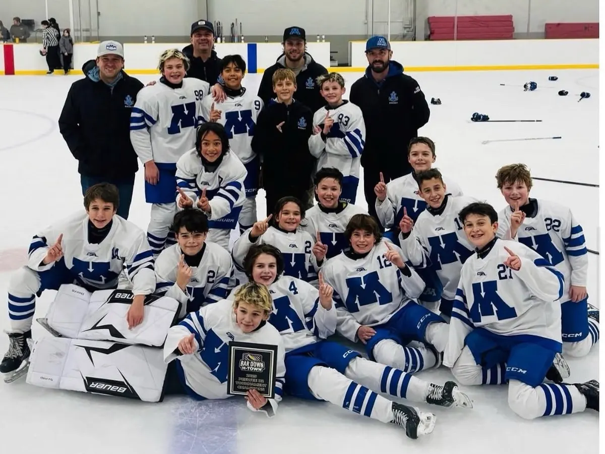 A Minnetonka boys team in white M jerseys celebrating on the ice with its coaches