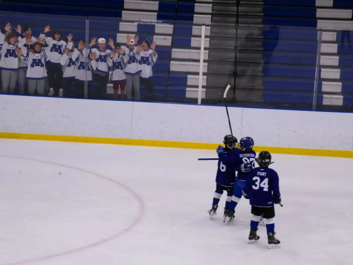 Minnetonka fans in white M jerseys cheering from the stands as three players celebrate a goal