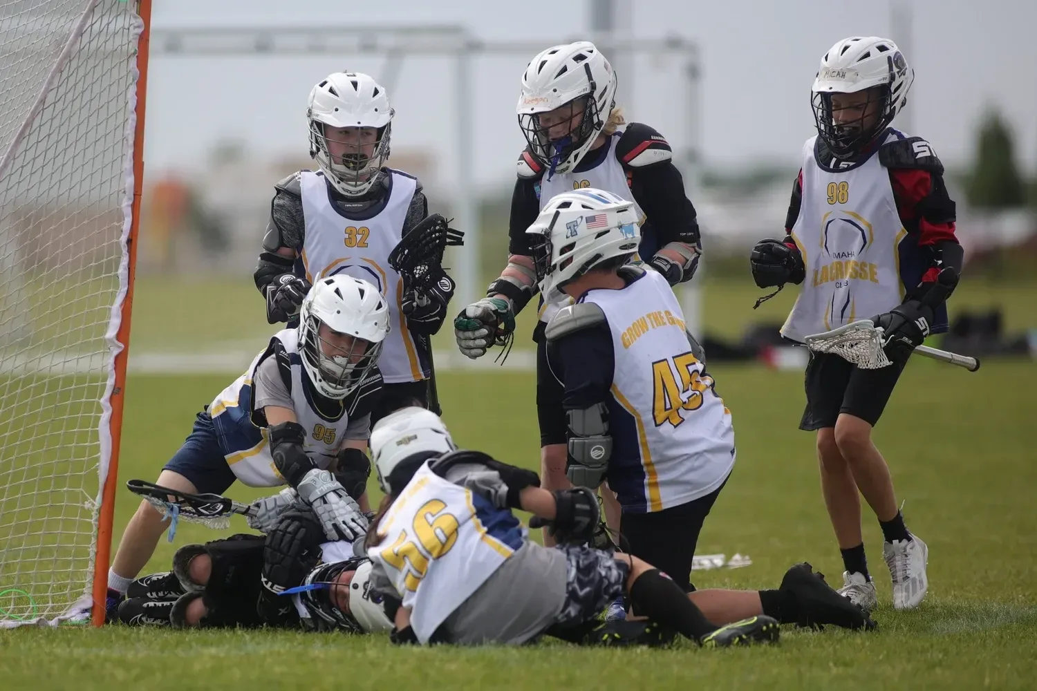 Omaha Lacrosse Club players in white jerseys around the goal