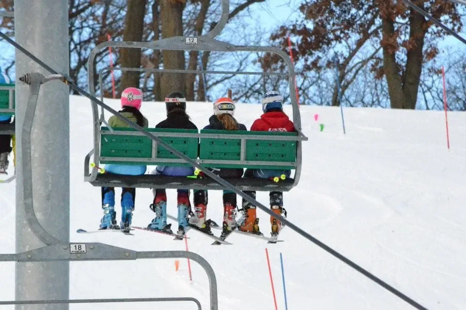 Four racers riding the chairlift, seen from behind